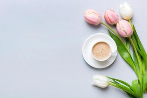 Spring background with flowers, cup of coffee and a bouquet of pink and white tulips on colored table background with place for text. Copy space top view photo