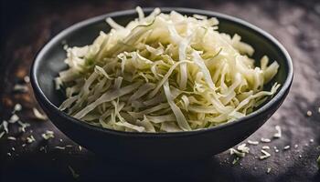 Bowl of thinly sliced raw cabbage with dramatic shadows on a dark table photo
