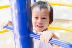 Child Boy beams with joy as he explores the playground, clutching onto a blue metal climbing frame. Kid innocent eyes sparkle with delight as he embarks on a playful journey. Playtime Adventure. photo