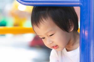 Asian young child gazes with curiosity, peering out from beneath a playful playground structure, a picture of innocent wonder and exploration. Closeup Curious kid boy. photo