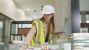 Confident architect in hardhat using laptop while analyzing office complex model at workplace video