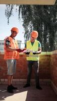 Two engineers wearing safety helmets are having a discussion on a construction site. Construction of a house. Engineers and architects review the construction video