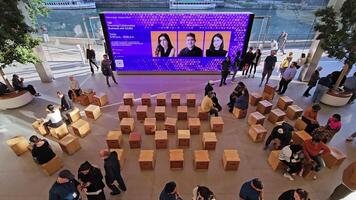 Chicago. Illinois 03.03.2025 Apple Store event in Chicago with attendees gathering for a tech talk, modern interior design with wooden seating, large digital display showcasing speakers, and a scenic video