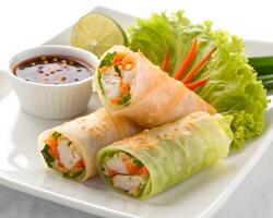 Close up of fresh spring rolls with lettuce and dipping sauce on a white square plate setting photo