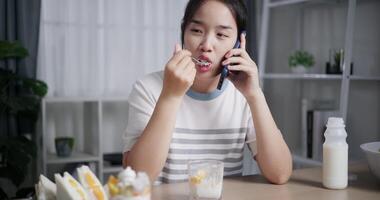 Handheld shot, Young woman enjoying food while talking on mobile phone with friend in living room at home. video