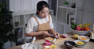 Handheld high angle view shot, Happy Asian woman using knife to cut dragon fruit on wooden cutting board at table. video