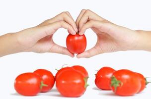Focus on ripe tomato in hands clasped in heart shape on blur of bunch of tomatoes on white background, conveying the message of love for eating vegetables and tomatoes. photo