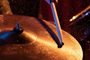 Drum sticks hitting snare drum with splashing water on dark background with orange and blue studio lighting. Dynamic scene. photo