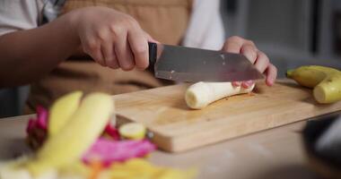 Handheld selective focus shot, Woman's hand using knife to cut bananas to prepare to make dessert on the table at home. video