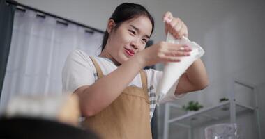 Handheld low angle view shot, Asian woman scooping whipped cream into a piping bag to prepare to make dessert on the table at home. video