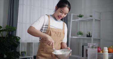 Handheld low angle view shot, young woman using a hand whisk to mix ingredients in a stainless steel bowl on a table at home. Cooking Concept ,Prepare food video