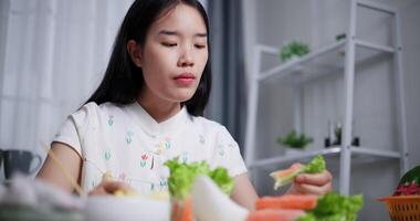 Handheld low angle view shot, Beautiful Asian woman enjoys delicious salad rolls at the dining table in home. Enjoy healthy food video