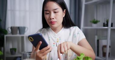 Beautiful woman enjoys eating fruit while playing with mobile phone happily at home. Relax at home, Enjoy healthy food video