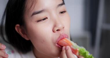 Handheld close up shot, Face of Young Asian woman enjoys delicious salad rolls at the dining table in home. Enjoy healthy food video