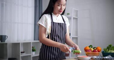 Handheld low angle view shot, A woman is peeling a cucumber with a vegetable scraper. Beautiful Asian woman preparing fresh vegetables to make salad rolls. video