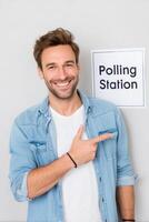 atractivo hombre sonriente y señalando a votación estación firmar promoviendo cívico participación y votación conciencia en un simpático ambiente votación concepto foto