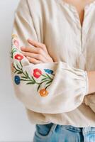 Close-up of a person wearing a light-colored embroidered blouse with floral designs on the sleeves, showcasing intricate craftsmanship and a relaxed, casual style photo