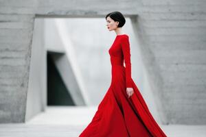 Elegant figure in flowing jester red dress walks gracefully through modern architectural space, showcasing a blend of fashion and contemporary design elements in a striking composition photo