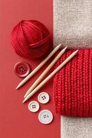 Jester red yarn ball, knitting needles, and buttons arranged on a textured surface, showcasing vibrant colors and crafting materials for creative projects and textile art photo