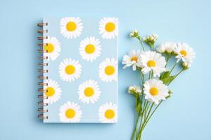 Colorful notebook with daisy pattern placed on a blue background alongside fresh white flowers, creating a cheerful and vibrant workspace atmosphere for creativity and inspiration photo