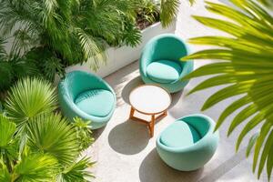 Stylish outdoor seating area featuring three modern turquoise chairs arranged around a wooden table, surrounded by lush greenery and tropical plants, creating a serene atmosphere photo