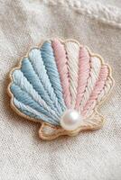 Embroidered shell patch featuring pastel colors of blue, pink, and cream, adorned with a pearl, showcasing intricate stitching on a textured fabric background photo