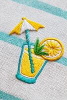Embroidered illustration of a refreshing yellow drink with a straw, lemon slice, and umbrella, set against a textured background, evoking summer vibes and relaxation photo