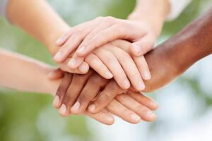 Diverse hands of different skin tones are stacked together in a symbol of unity and collaboration, showcasing teamwork and solidarity in a vibrant outdoor setting photo