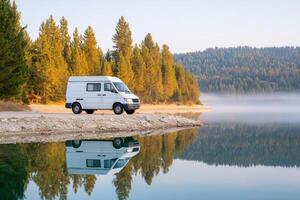 White camper van parked by serene lake surrounded by lush green trees, reflecting in calm water, showcasing peaceful outdoor adventure and exploration photo
