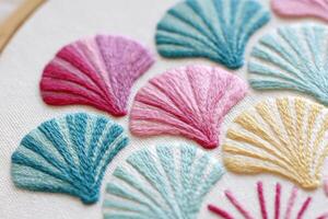 Colorful embroidered shells in various shades of pink, blue, and yellow arranged on a textured fabric background, showcasing intricate stitching and artistic craftsmanship photo