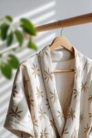 Elegant cream robe with intricate floral patterns hanging on a wooden hanger, illuminated by soft natural light, creating a serene and inviting atmosphere in a modern interior space photo