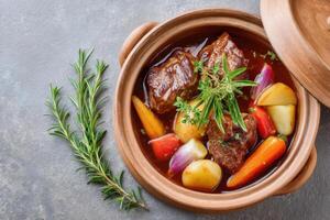 Terracotta pot containing slow-cooked lamb stew with potatoes, carrots and aromatic herbs photo
