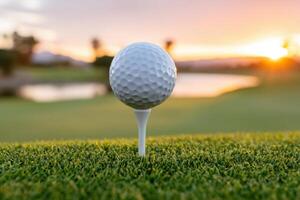 Golf ball positioned on a tee, surrounded by lush green grass, with a serene sunset reflecting on a calm water body in the background, creating a tranquil golfing atmosphere photo