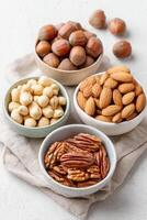 Assorted nuts in bowls, including almonds, pecans, hazelnuts, and macadamia nuts, arranged on a textured cloth, showcasing a healthy snack option and natural food presentation photo