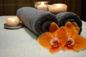 Rolled towels, orchid flowers, and lit candles creating relaxing spa ambiance photo