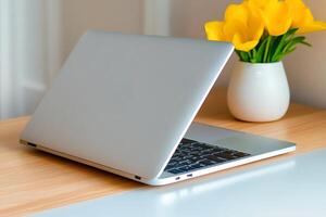Modern silver laptop showing keyboard and trackpad with yellow flowers on desk photo
