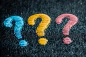 Three colorful question marks symbolizing uncertainty and curiosity on dark background photo