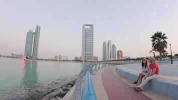 sunset timelapse couple visitors enjoy relaxed moment sit on bench enjoy sunset by Etihad Towers in Abu Dhabi, architecture with public space and modern city life video