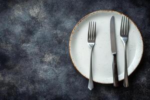 Empty plate with knife and forks on dark background table setting photo