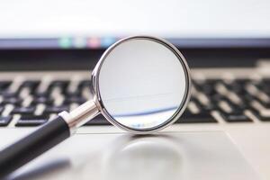 Magnifying glass resting on laptop keyboard exploring digital world photo