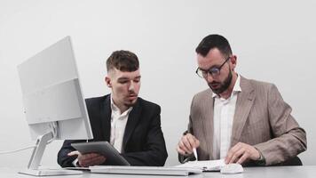 Two business men discuss an online project or presentation at a computer with a tablet. Focused coworkers work in pairs at a computer using apps. The concept of teamwork and brainstorming. video
