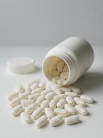 White tablets spilling from an open plastic bottle on a clean white background. Perfect for illustrating medication use, pharmaceutical content, healthcare articles, or drug safety campaigns. photo