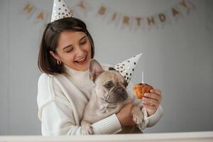 Celebration of birthday. In hats and with cake. Young woman is with her,, pug dog at home photo