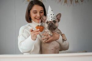 Happy birthday. Pet in hat and with cake. Young woman is with her pug dog at home photo