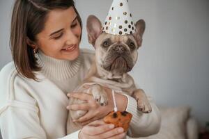 Celebration of birthday. In,, hats and with cake. Young woman is with her pug dog at home photo