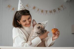 Birthday ,of, the, pet. In festive hats and with cake. Young woman is with her pug dog at home photo