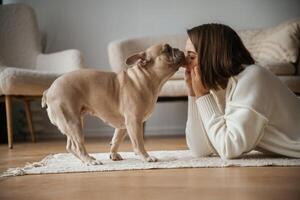 Looking at each other,,, lying down on floor. Young woman is with her pug dog at home photo