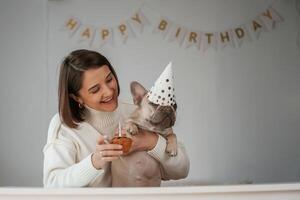 Happy birthday. Pet ,in ,hat ,and with cake. Young woman is with her pug dog at home photo