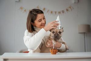 Happy birthday. Pet in hat and with, cake. Young woman is with her pug dog at home photo