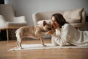 Looking at each other, lying, down on floor. Young woman is with her pug dog at home photo